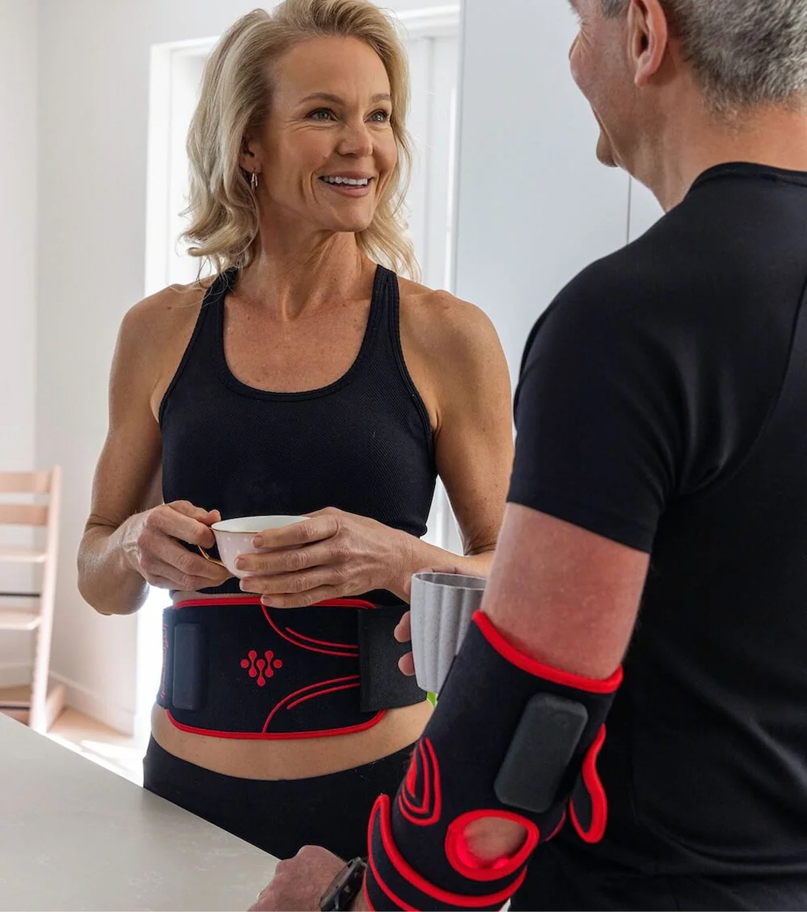 Two people wearing fitness gear, holding cups, and smiling indoors.
